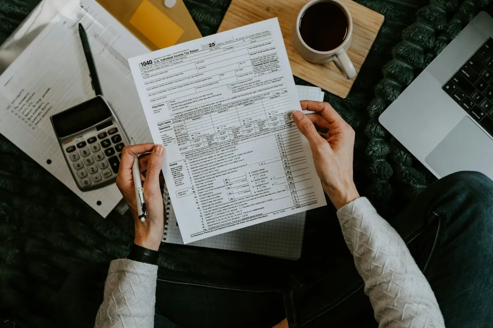 Moduli, calcolatrice e caffè su una scrivania, visti dall'alto